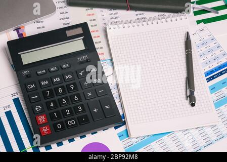 Calculator and an empty Notepad page on the office Desk with financial indicators and charts. Top view with a copy of the text input space. Finance Stock Photo