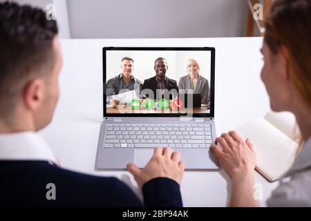 Rear View Of Businesspeople Video Conferencing With Their Colleagues On Laptop Over White Desk Stock Photo