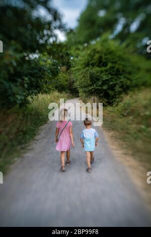Brother and sister walking together on a narrow paved path in the countryside in summer Stock Photo