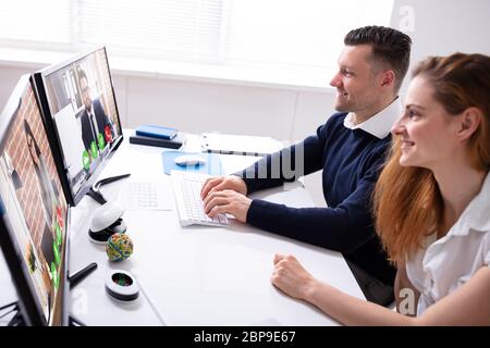 Side View Of Businesswoman And Businessman Video Conferencing With Colleagues On Computer In Office Stock Photo