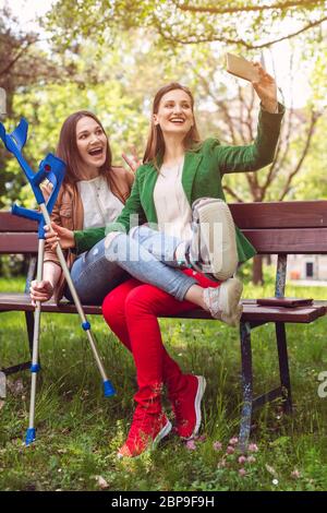 Best friends with one having a broken leg taking a selfie on the phone Stock Photo