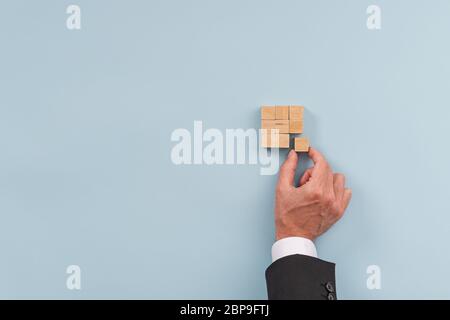 Hand of a businessman building a squared structure of wooden blocks in a conceptual image of business vision, strategy and start up. Over blue backgro Stock Photo