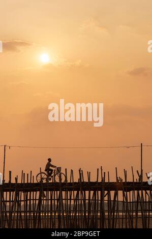 A cyclist crossing the Bamboo bridge at sunset. Ko Pen, Cambodia, Southeast Asia Stock Photo