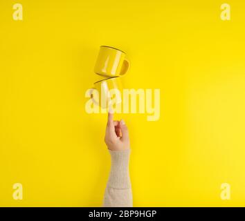 two yellow ceramic cups are supported by a female hand on a yellow background, copy space Stock Photo