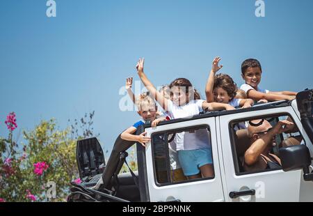 Happy children having fun in the car, cheerful kids standing in the open-top vahicle, enjoying summertime road trip Stock Photo