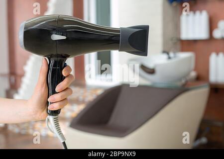 Hair dryer professional hair dresser tool in hairdresser's hand against beauty salon interior background. Hair stylist work space. Beauty hairdressing Stock Photo