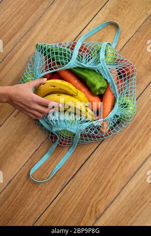Woman's hand holding a banana of a Cotton string eco bag with fruits and vegetables on wooden background Stock Photo