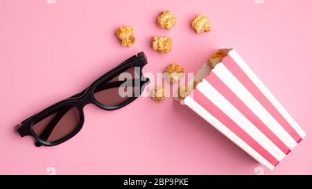 Popcorn in red and white cardboard box and 3d glasses on pink background. Watching movie with pop corn concept. Flat lay, top view. Stock Photo