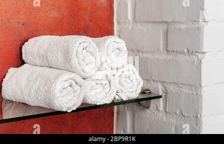 White towels in rolls on shelf in bathroom, beauty salon or hotel. Cotton towel for spa hair, body . Relaxation, hygiene, hair care at home Bathroom Stock Photo
