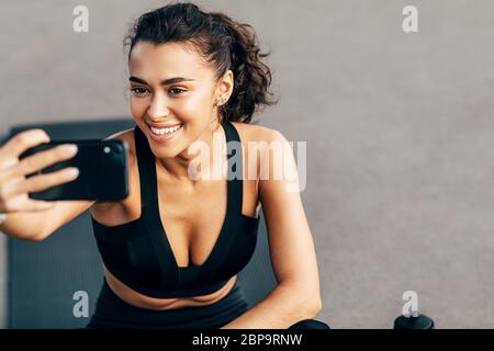 Close up of a beautiful smiling woman holds a cell phone and taking selfie after training Stock Photo