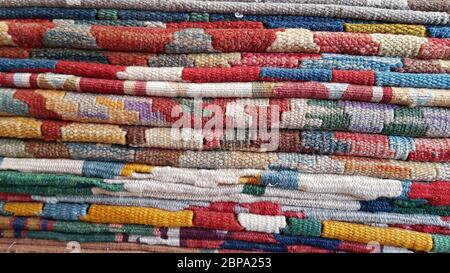 Layers of colorful folded carpets with bright ornaments. Stack of vintage Turkish carpets closeup. Woven texture. Edges of ethnic rugs background. Tra Stock Photo