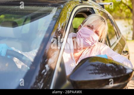Elderly woman wearing a face mask while driving a car for corona virus home visit during Covid-19 pandemic Stock Photo