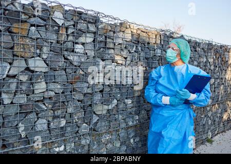 Nursing staff or containment scout waits in front of wall for visitors with list for contact tracking in coronavirus pandemic Stock Photo