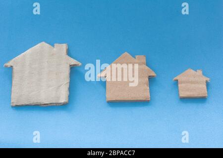Different Size Of Houses Arranged In Row on blue background. Three differently sized cardboard models of houses. Rent, purchase, delivery of housing a Stock Photo