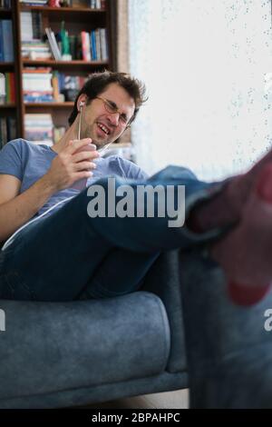Young man is  talking with his family on the smart phone from the room. He is happy and laughing. Stock Photo