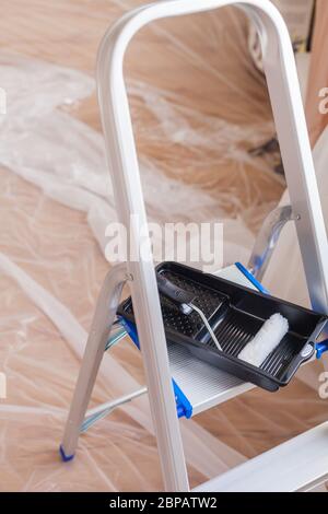 Aluminum ladder is folded out on the taped floor with drip tray craftsman renovation paint preparation do it yourself tools Stock Photo