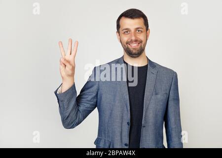 Young businessman with a beard smiles, male businessman in a stylish jacket showing the number three with his fingers, smiling confidently and happy looking at the camera Stock Photo