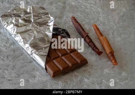 A bar of open chocolate and two pieces of fruit candy on a white fleecy background. Chocolate in foil and sweets wrapped in a scroll. Naturally health Stock Photo