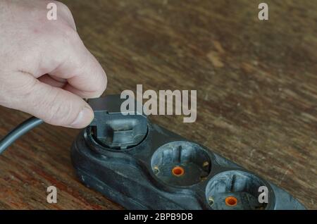 Incorrect disconnection of the electrical plug from the extension cord. Incorrect hold of the electric plug in the hand. A worker disconnects a power Stock Photo
