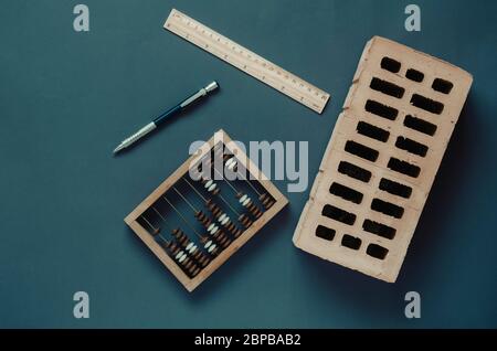 Building industry accounting background. Creative background with thematic objects on a dark turquoise background. Wooden abacus, red brick, ruler and Stock Photo