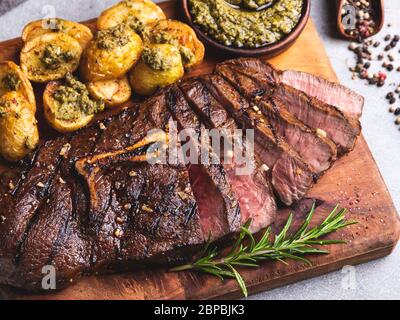 Sliced juicy steak medium rare beef on the bone with roasted new potatoes pesto sauce Stock Photo