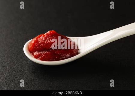 Classic tomato ketchup in a white chinese porcelain spoon on a black stone serving board. Sauces and seasonings for meat, fish and vegetables. Stock Photo