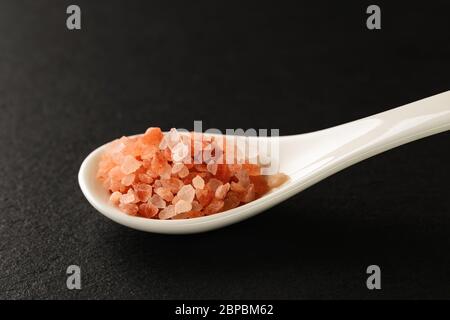 Pink himalayan salt in a white chinese porcelain spoon on a black stone serving board. Sauces and seasonings for meat, fish and vegetables. Front view Stock Photo