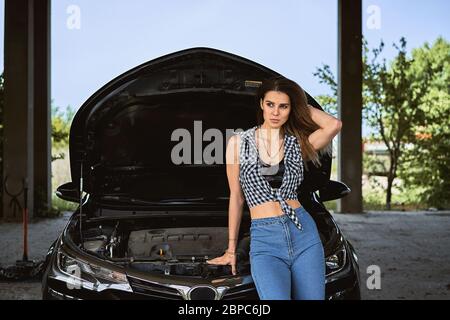 girl is standing next to the car with the hood open Stock Photo
