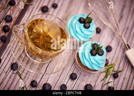 Chocolate cupcakes with blueberries. Cupcakes and a cup of tea on a table with blueberries and a whisk. Selective focus. Stock Photo