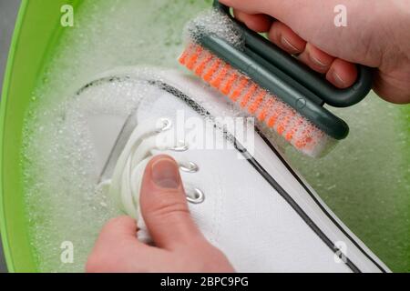 Man cleaning white canvas sneakers, close up Stock Photo