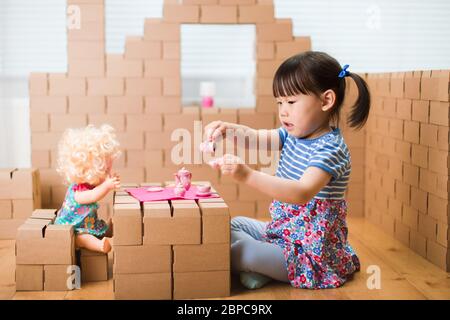 toddler girl pretend play baby care in a carton house Stock Photo