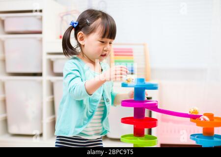 toddler girl play marble run game at gome agianst white background Stock Photo