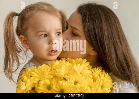 motherhood, mothers day, birthday, childhood, family concept - close-up little girl in dress congratulate and give young mother bouquet of yellow Stock Photo