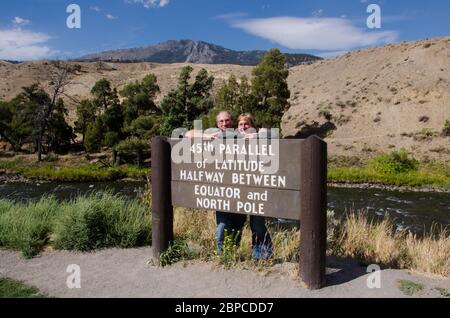 An senior adult couple pose at the 45th parallel sign in Yellowstone National Park Stock Photo