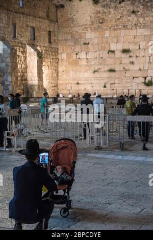 An ultra-orthodox ('Charedi') man, with a surgical mask, photographs his child near the famous Western Wall in Jerusalem, where access have been limited and dividers erected in order to limit the spread of the Covid-19 Coronavirus. Stock Photo