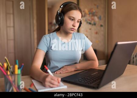 teenage girl, writes pen home with headphones, notebook, listens to lessons and learns on the Internet, a laptop with the Internet. Distance education Stock Photo