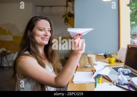 Focussed paper airplane in female hand. Blurred woman woman launches paper airplane sitting at her workplace with laptop, blanks for ideas, colorful s Stock Photo