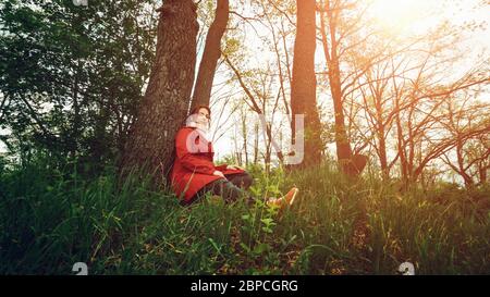 Young pretty woman in red coat having rest in spring forest and looks at camera. Stock Photo