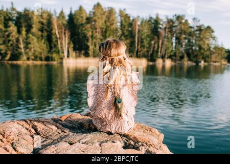 young girl sat on a rock with feathers in her hair thinking