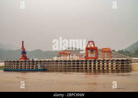 Huangqikou, Chongqing, China - May 8, 2010: Yangtze River. Landscape of rred cranes on multi-level port quay behind brown water. Barge docked, Green f Stock Photo