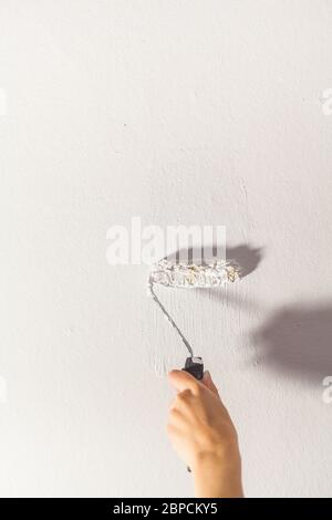 Human hand with small paint roller starts painting white wall craft painter training tools Stock Photo
