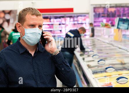 Portrait of a young caucasian businessman in a protective mask is talking on the phone in a hypermarket. Stock Photo