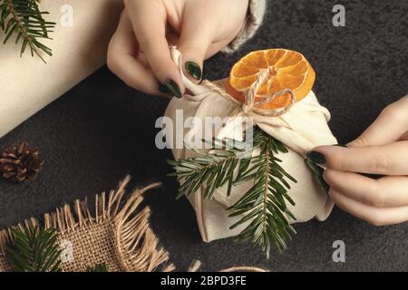 Zero waste and eco friendly christmas concept. Female hands wrap gifts in natural fabric with ornaments made of natural materials. Stock Photo