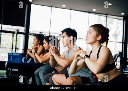 Group of athletic young Asian people in sportswear doing squat and exercising at the gym. Intense workout and healthy lifestyle concept Stock Photo