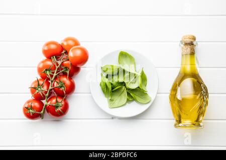 Cherry tomatoes, basil leaves and olive oil in bottle on white table. Top view. Stock Photo