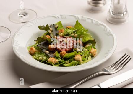 Green salad with lettuce tomatoes on white blurred background with wine glasses, vinegar and olive oil. Stock Photo