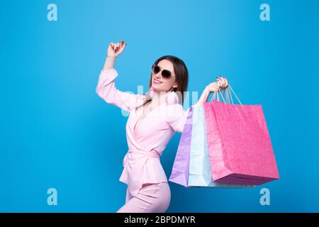 A fashionably dressed girl in sunglasses with multi-colored shopping bags is happy with the discounts and sale. Isolated on a blue background Stock Photo