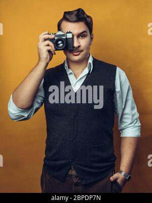 Young Handsome Man Holding Film Camera Near Face, Portrait On Yellow Background Stock Photo