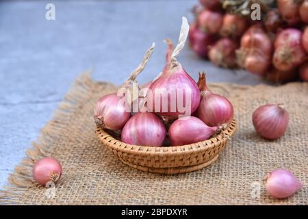 Thai red onion or Shallots. Fresh purple shallots on bamboo basket with old wallpaper and shallots bunch background. Selected focus. Concept of spices Stock Photo