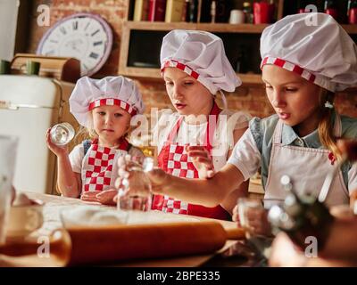 Three little chefs enjoying in the kitchen making cakes. Girls at the kitchen. Family housekeeping. Stock Photo